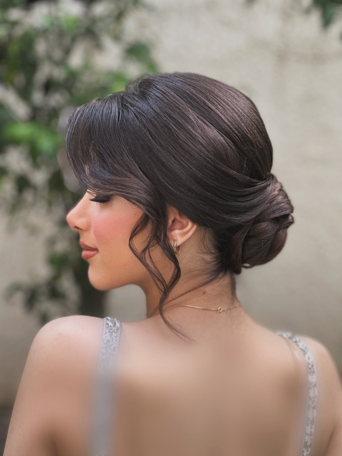 Woman with polished dark hair twisted into a low chignon and loose tendrils