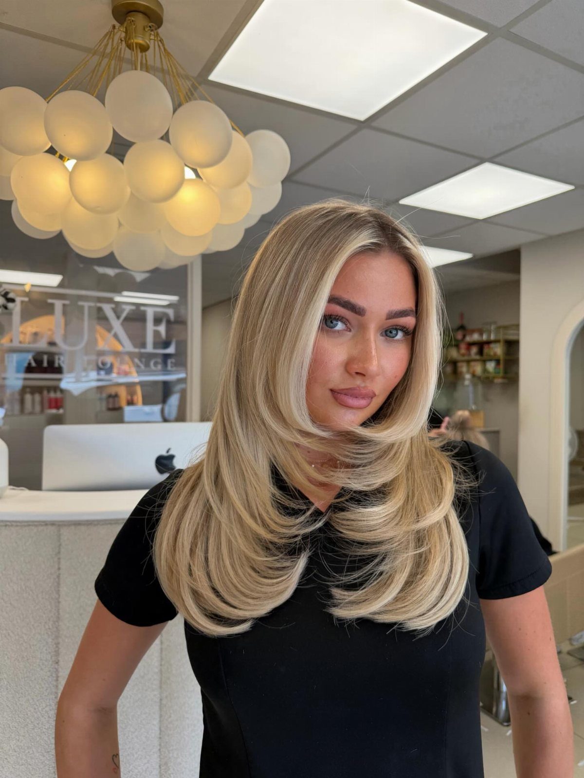 Woman showing a smooth, voluminous blonde blowout with curled-under layers in a salon