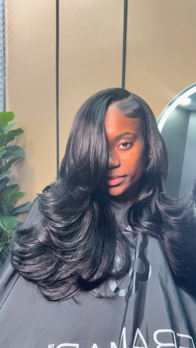 Long black layered hair falls in glossy sweeping curls over a salon cape