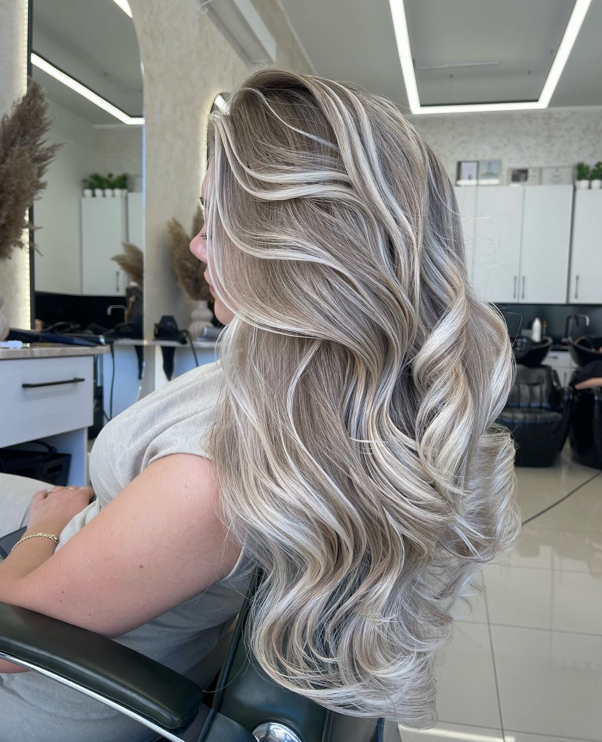 Woman displaying long silver-blonde waves in a bright modern hair salon