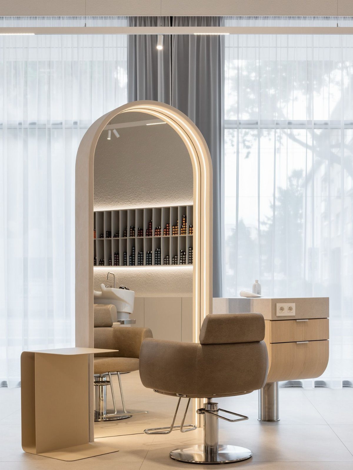 Beige salon station with an arched mirror, tan styling chair, and pale wood cabinets