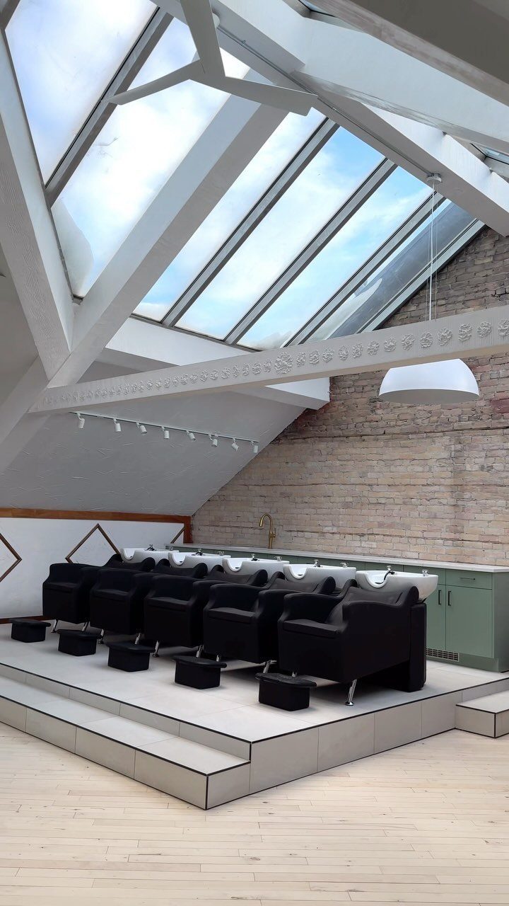 Black shampoo chairs and white basins beneath a bright salon skylight
