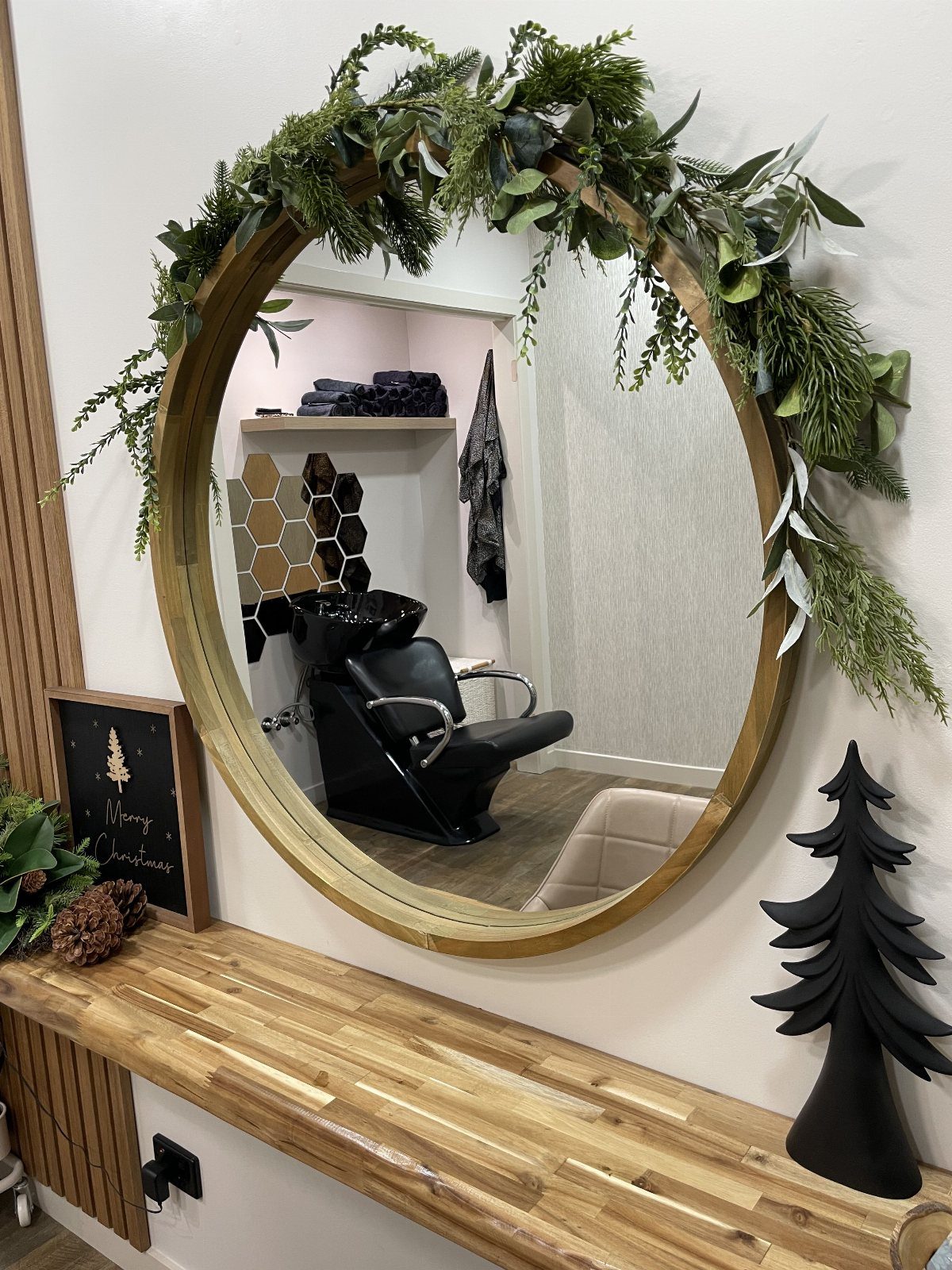 Round gold-framed salon mirror decorated with asymmetrical evergreen garland