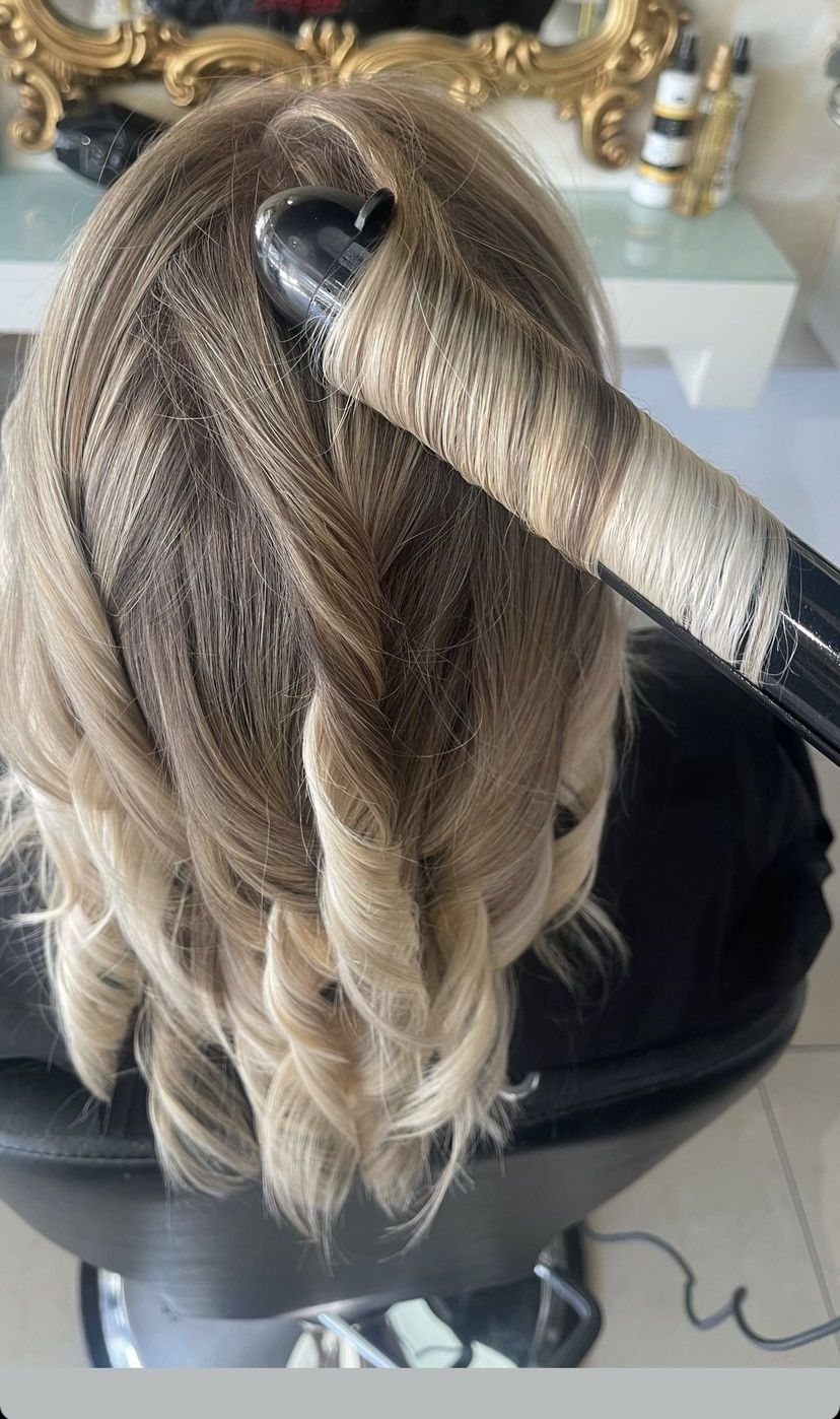 Highlighted long hair wrapped around a curling iron in a salon