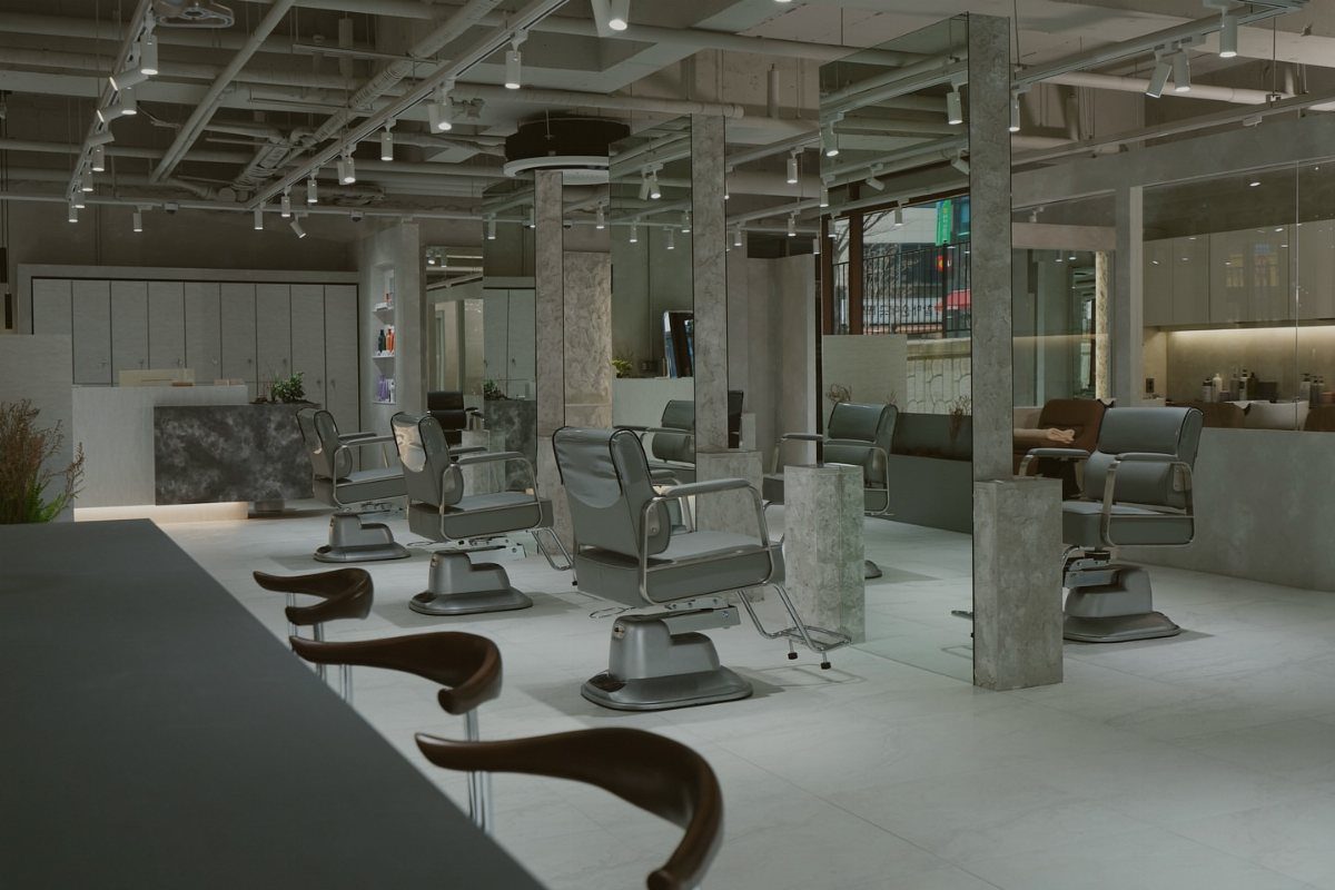 Industrial hair salon with exposed ducts, concrete floors, mirrors, and styling chairs