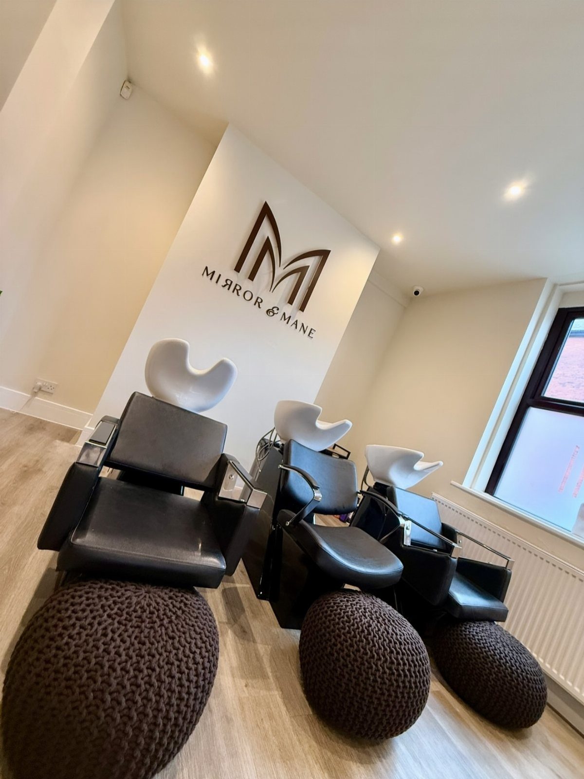 Modern hair salon with black shampoo chairs, basins, ottomans, and Mirror & Mane wall logo