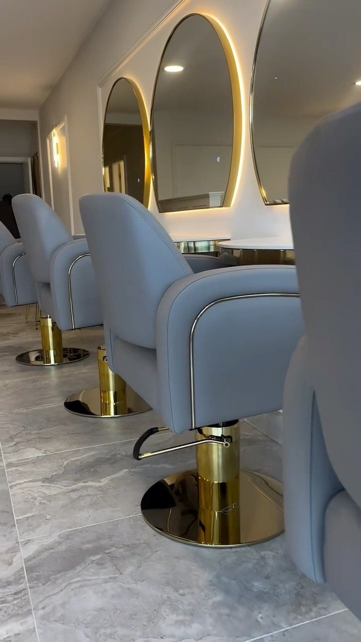Hair salon interior with pale blue chairs, arched mirrors, and gold accents