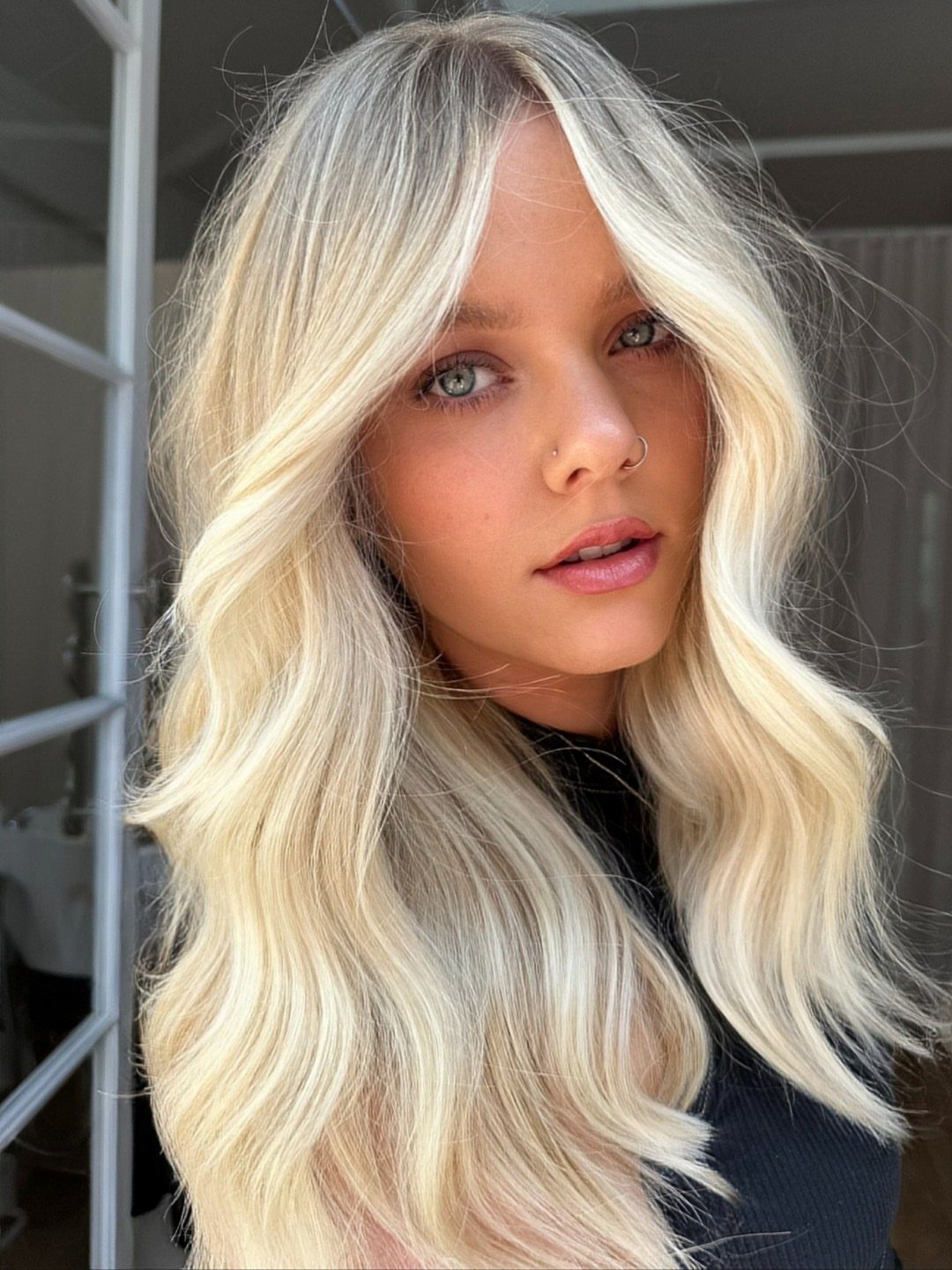 Woman with long, wavy platinum-blonde hair posing inside a salon