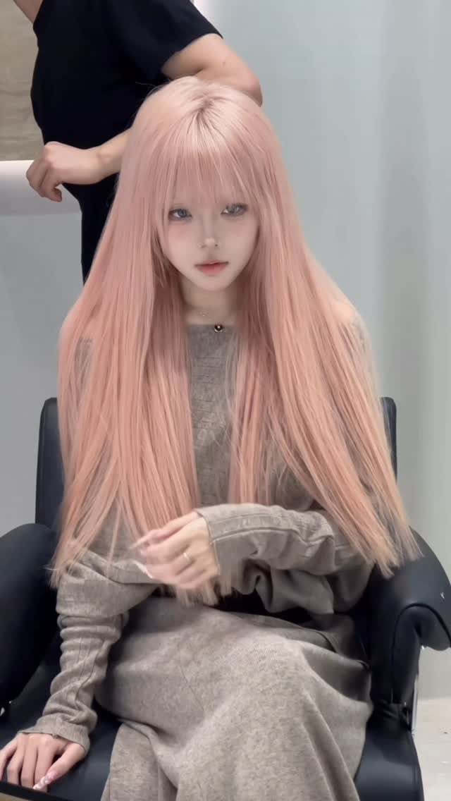 Person with long pastel pink hair sits in a black salon chair
