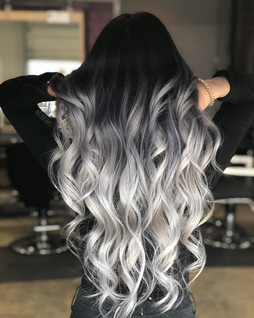 Long wavy silver-blonde balayage hair with dark roots in a salon