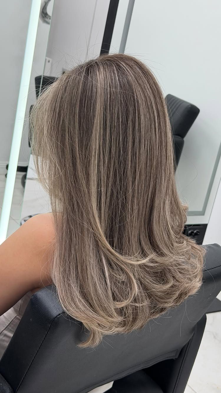 Long wavy ash blonde hair with a seamless balayage blend and dark roots.