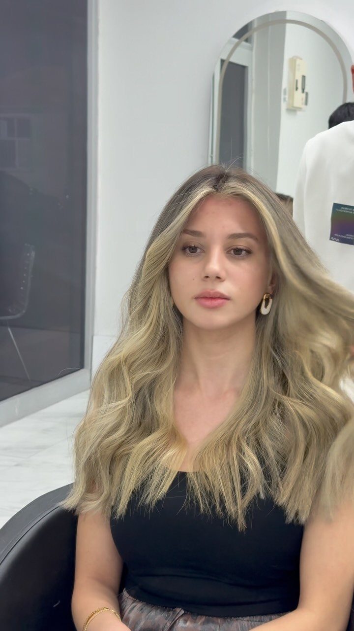 Woman with long wavy ash blonde hair featuring a dark to light ombre gradient.