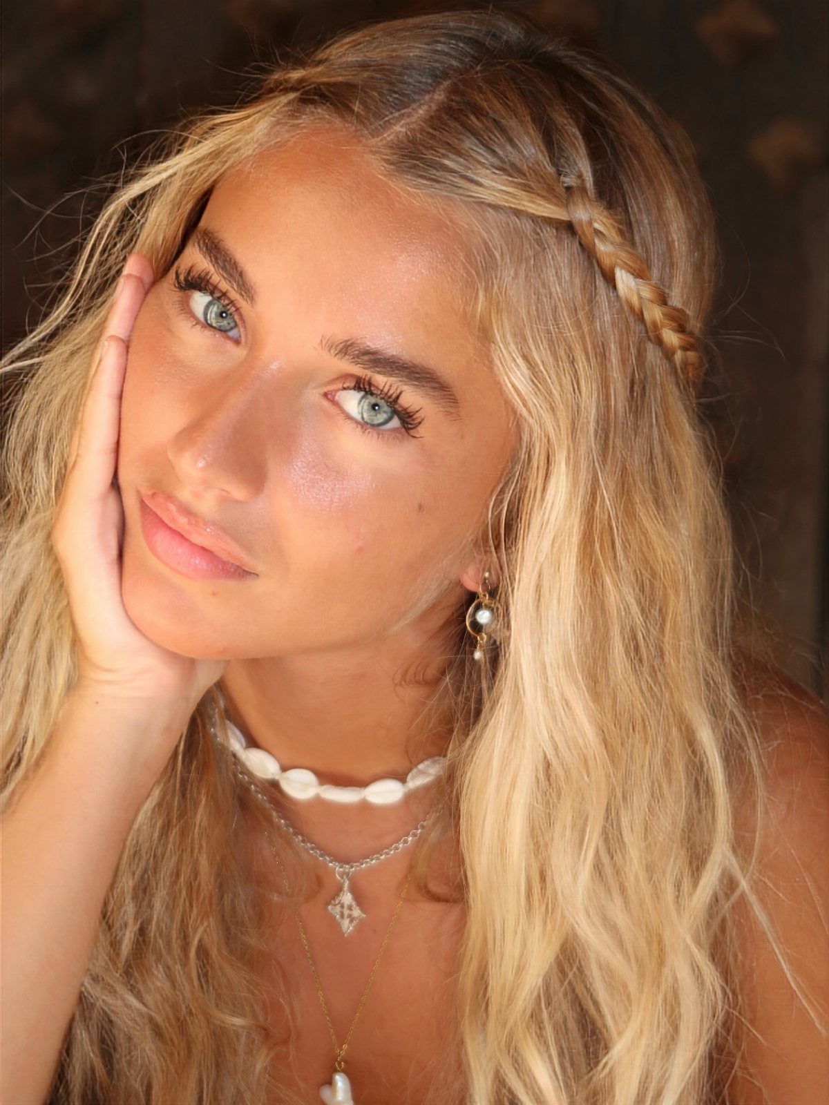 Woman with wavy ash blonde hair, a side braid, and shell necklace.