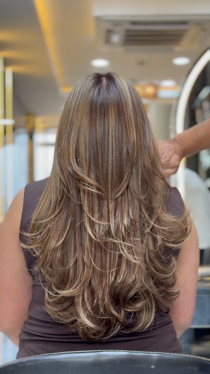 Long layered hair with caramel and ash blonde highlights styled in voluminous curls.