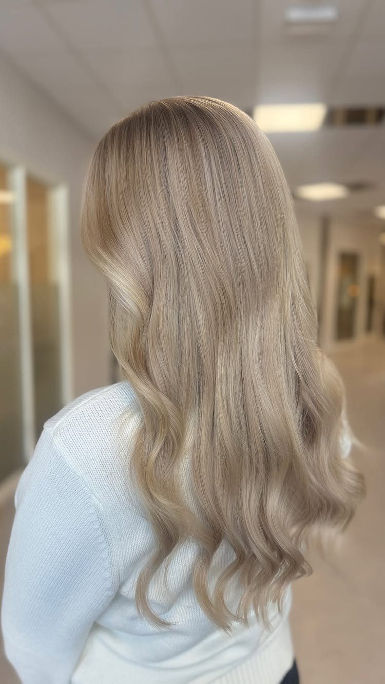 Long wavy champagne ash blonde hair on a woman wearing a white sweater.