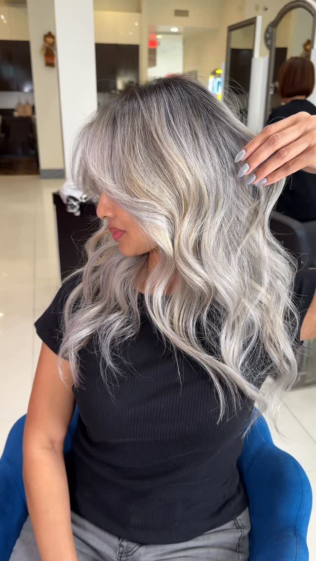 Woman with long wavy ash blonde hair and dark roots in a salon.