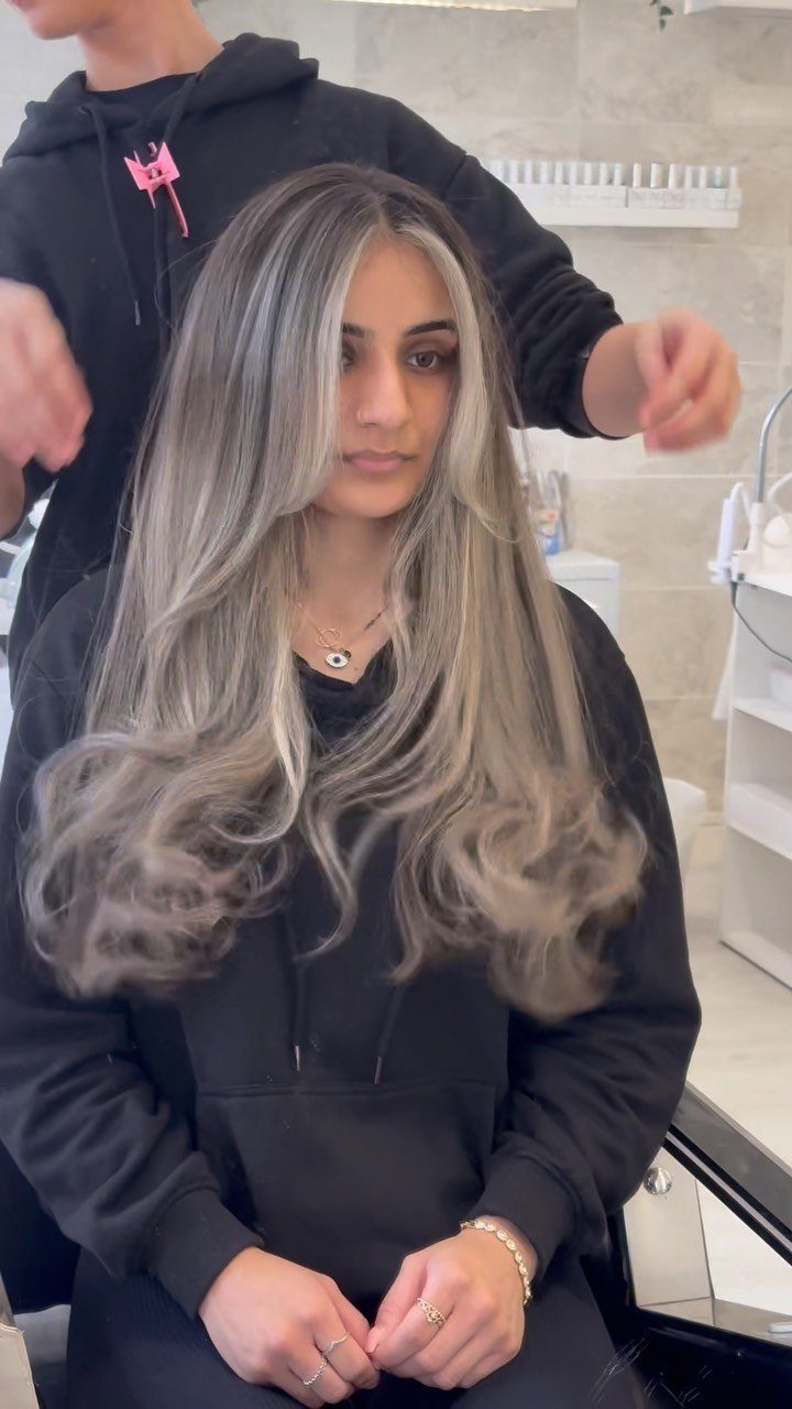 Woman with long wavy light ash blonde hair and dark roots in a salon.