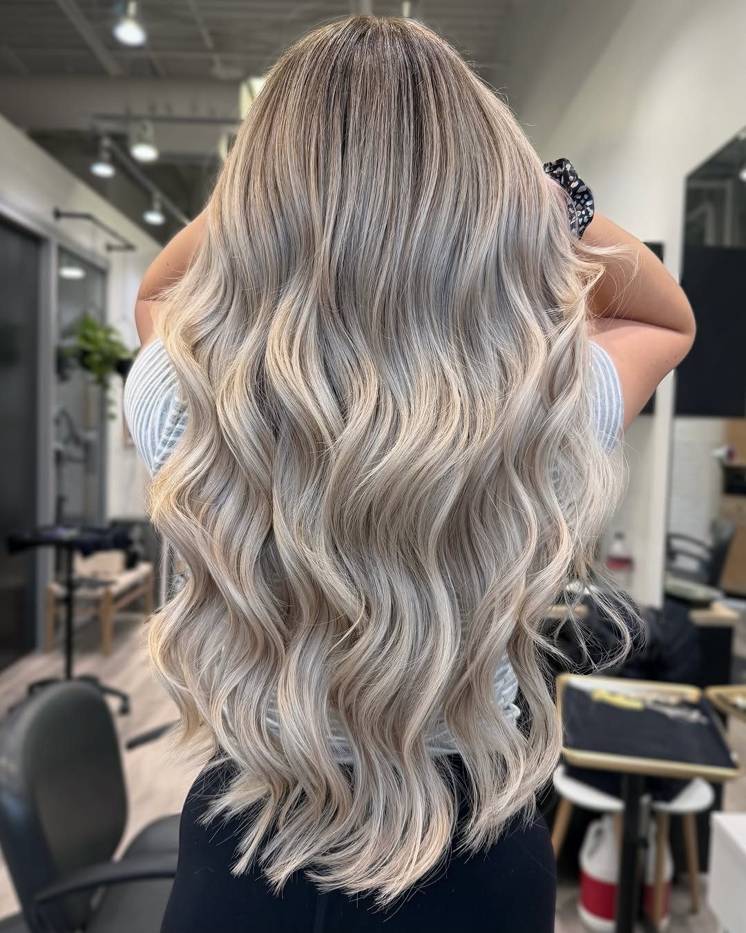 Long wavy pearl ash blonde hair with dark roots in a salon.