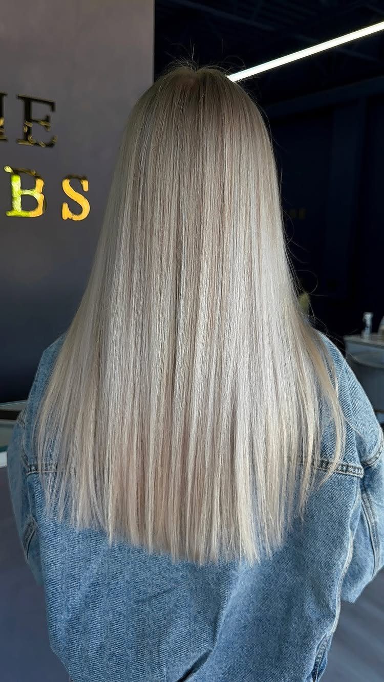 Long straight platinum ash blonde hair on a person wearing a denim jacket.