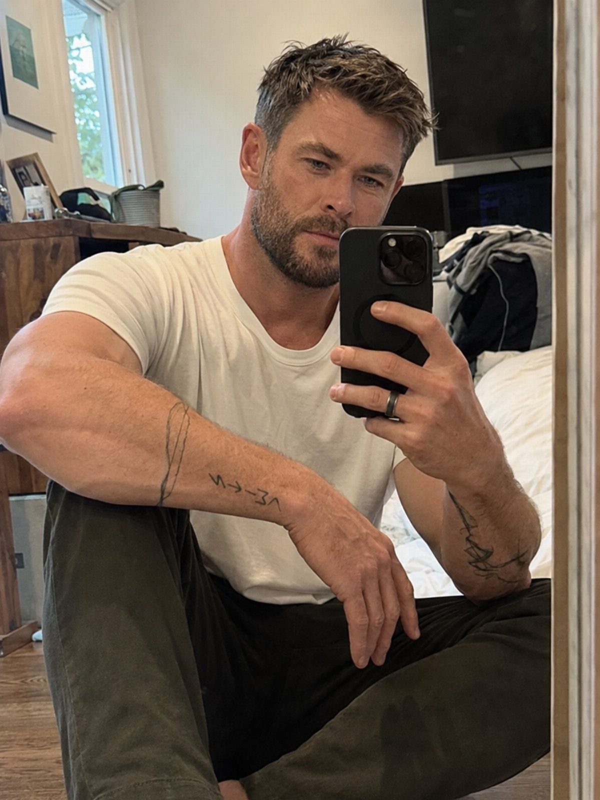 Man with short textured brown hair taking a mirror selfie in a white T-shirt