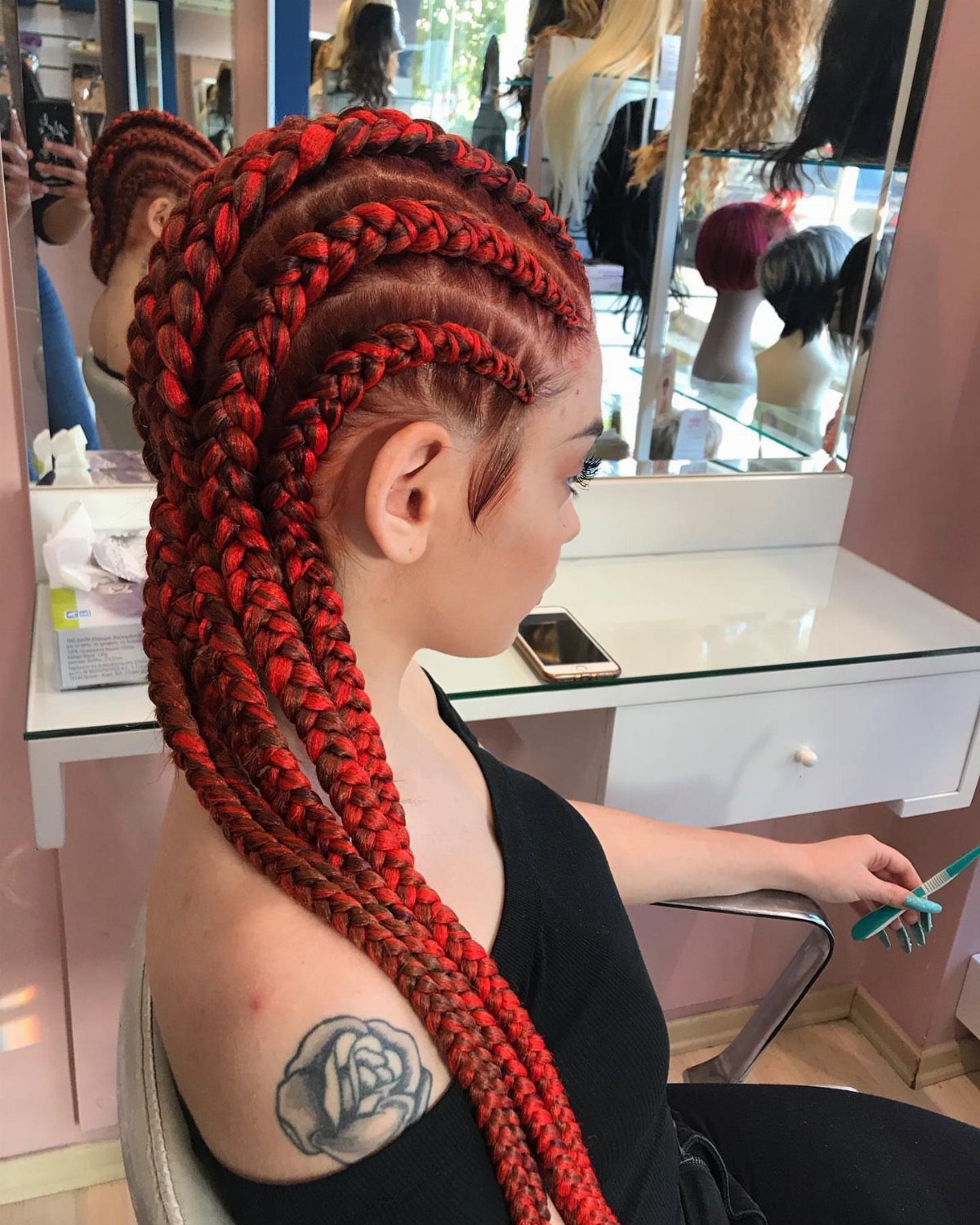 Woman showing long black and red cornrows with bright extensions in a salon