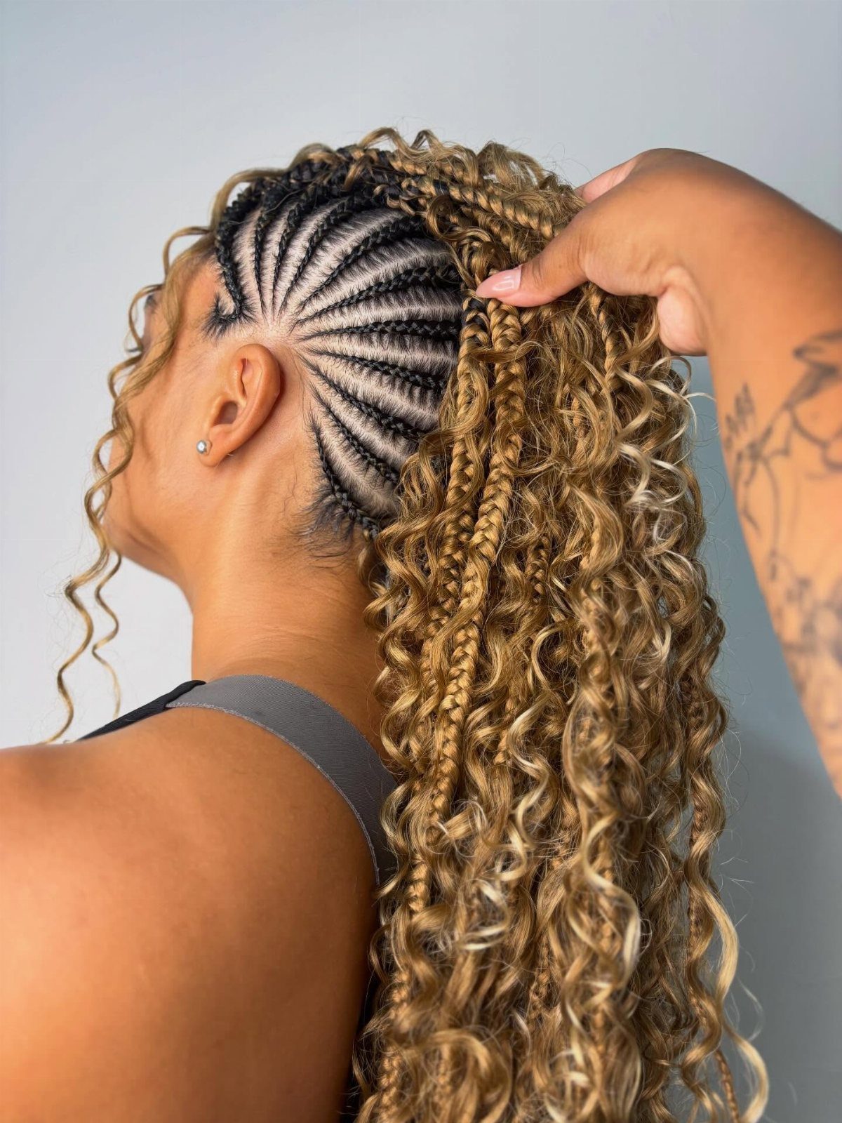 Cornrows sweep toward raised curly braids gathered along the center of her head