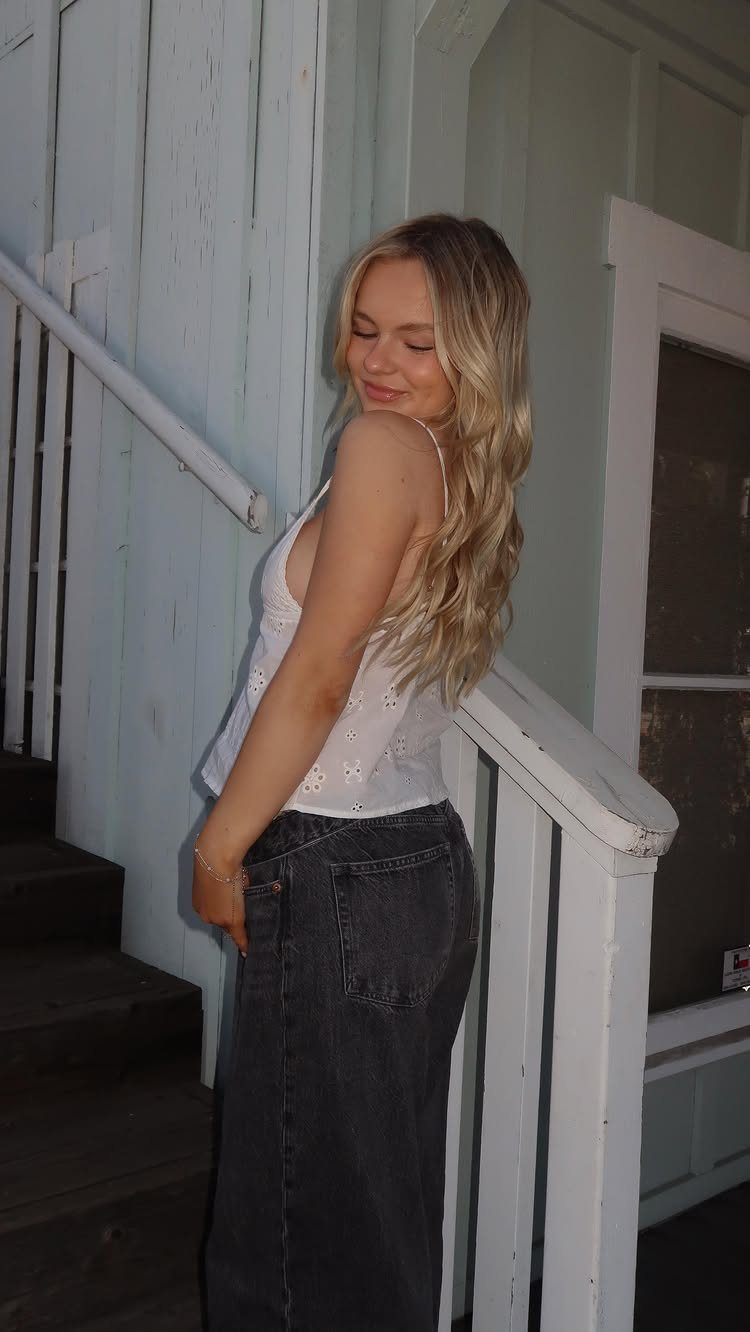 Young woman with long blonde beach waves posing beside a white staircase