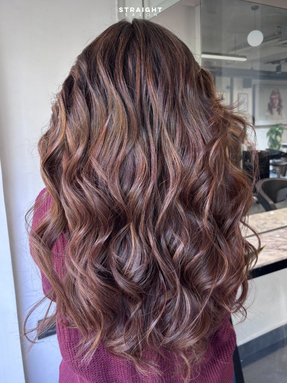 Long brunette hair styled in voluminous loose curls with subtle highlights