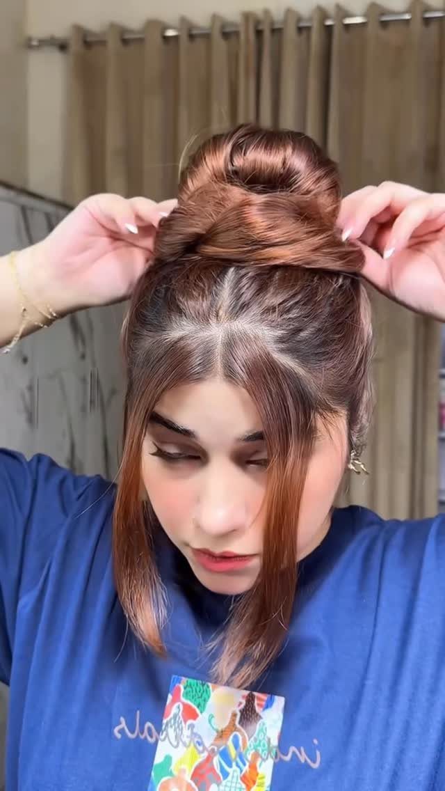 Messy top knot with loose face-framing strands as a woman adjusts her hair