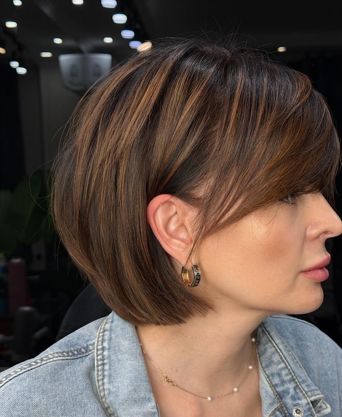 Woman with a sleek brown bob and long side-swept bangs in profile