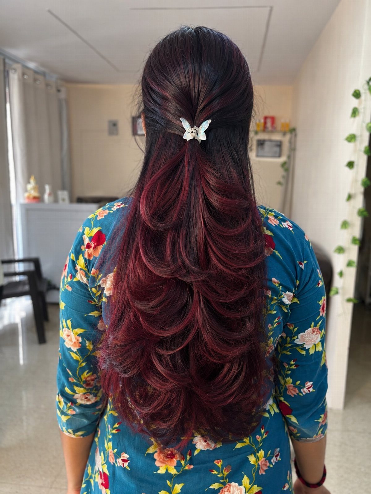 Long dark plum hair falls in glossy, layered feathered curls down the back.