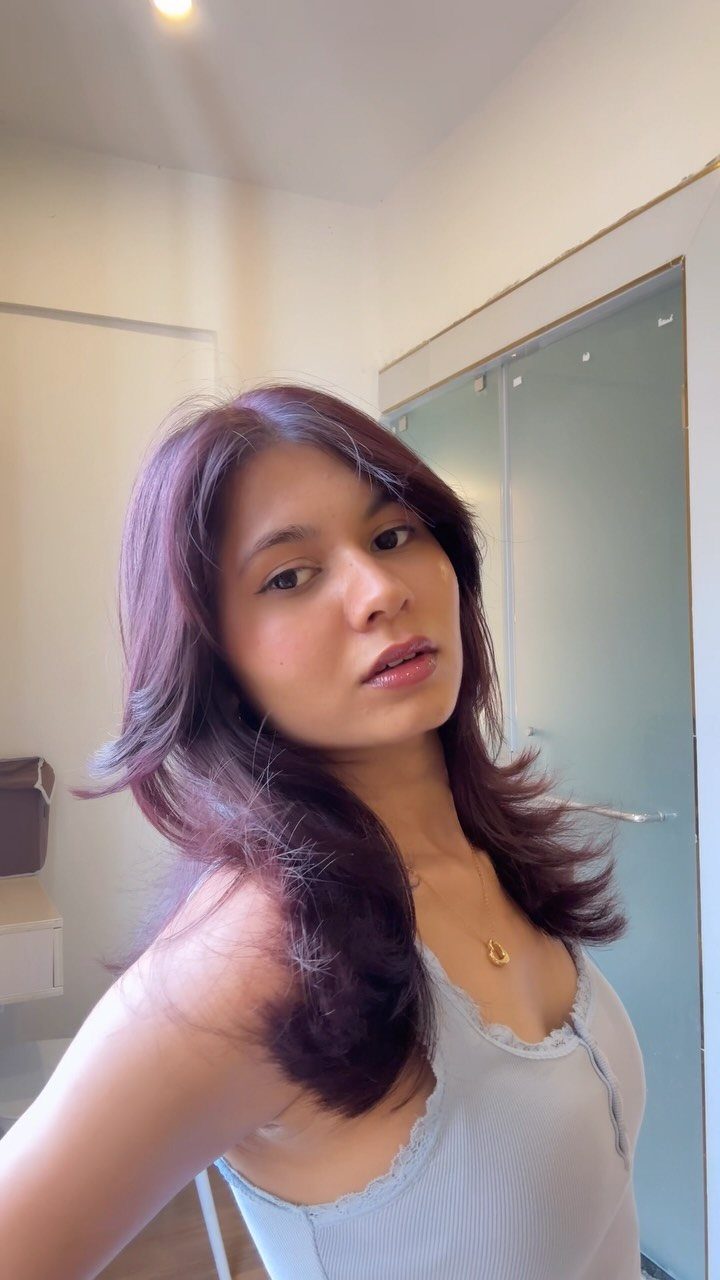 Woman with glossy dark plum hair in long, feathered layers