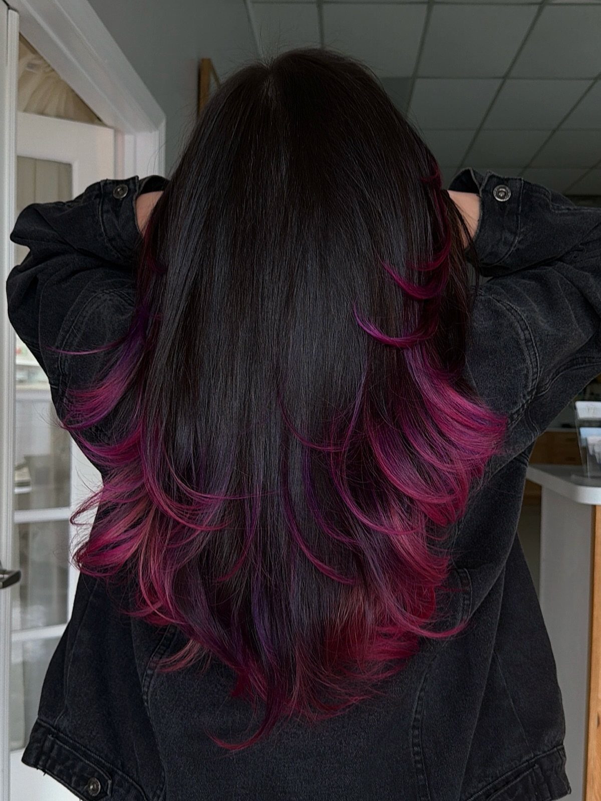 Long dark plum hair with magenta feathered layers curling outward at the ends
