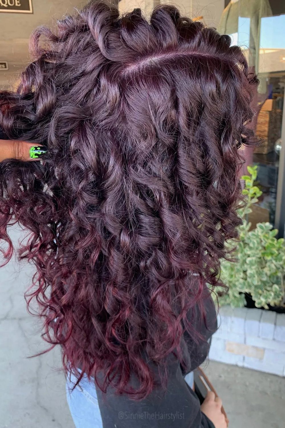 Shoulder-length plum curls show subtle red highlights throughout