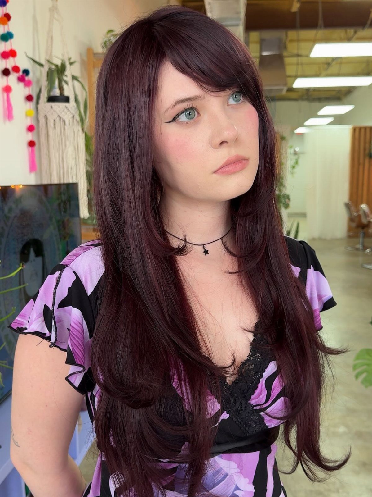 Woman with long, dark plum hair styled in a deep side part and side-swept bangs