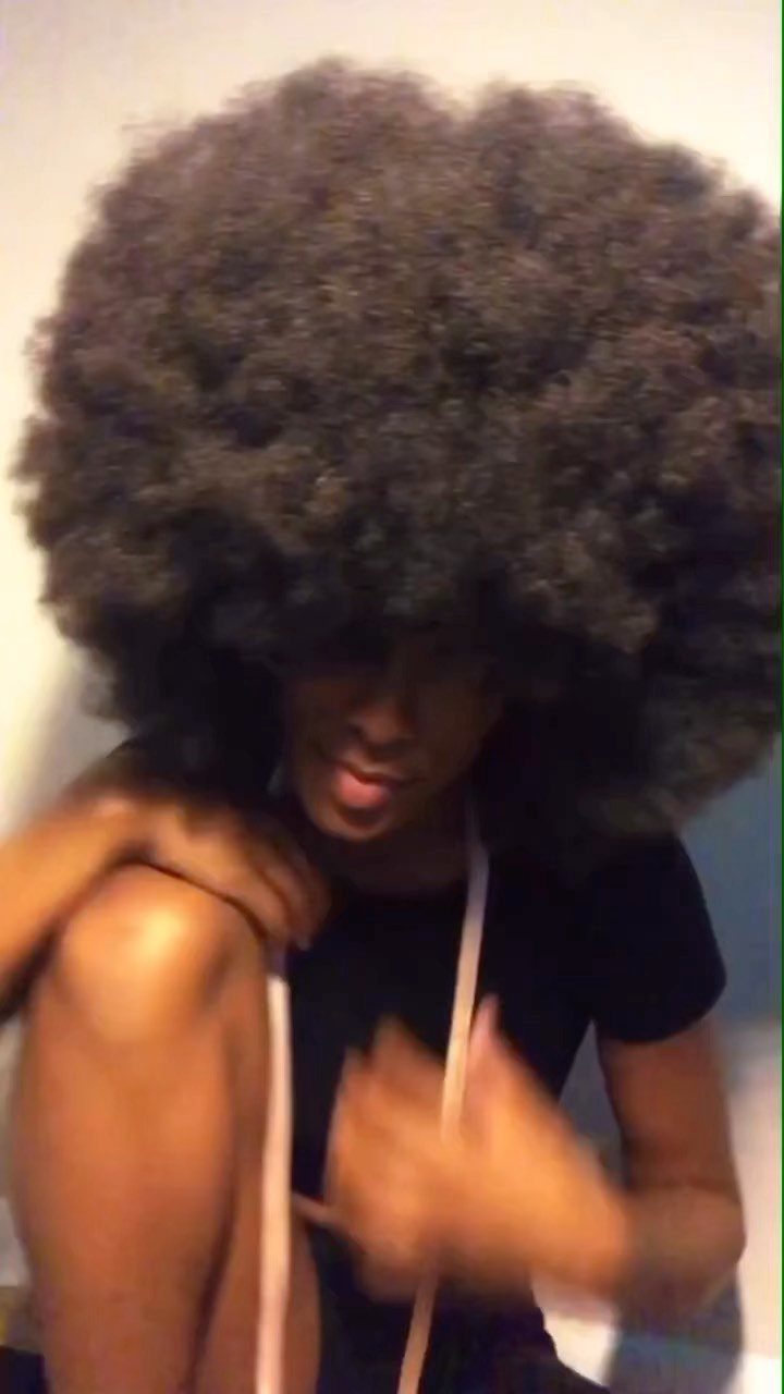 Large rounded natural afro frames a person leaning forward in a dark shirt