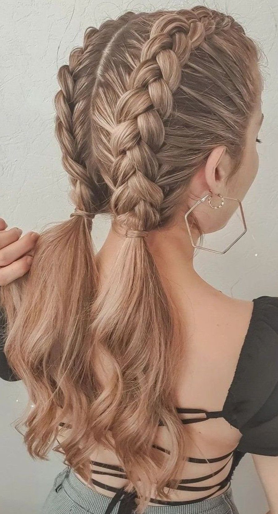 Two thick Dutch braids run down blonde hair into loose wavy ponytails