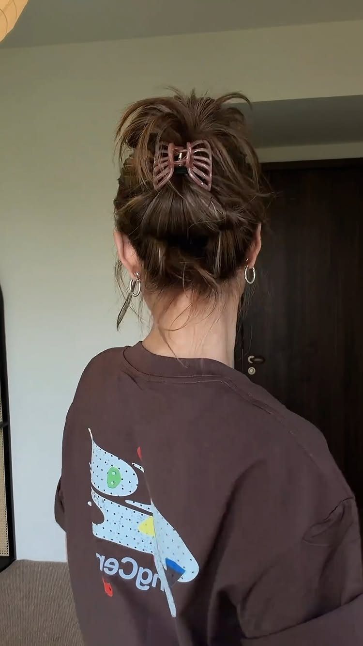 High messy bun secured with a pink claw clip on dark brown hair