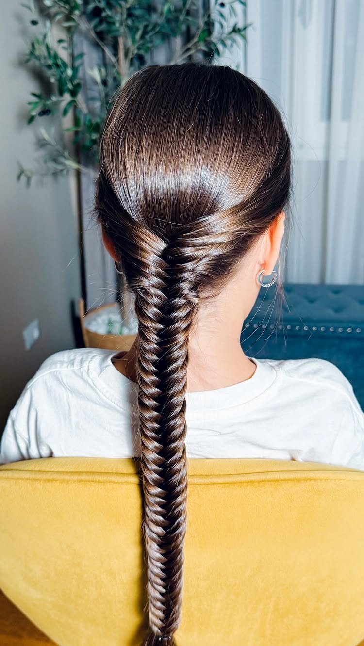 Long brown fishtail braid falls down the back of a person seated in a yellow chair