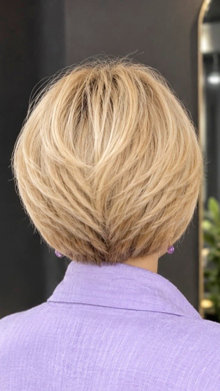 Short blonde layered bob haircut with feathered ends above a lavender top