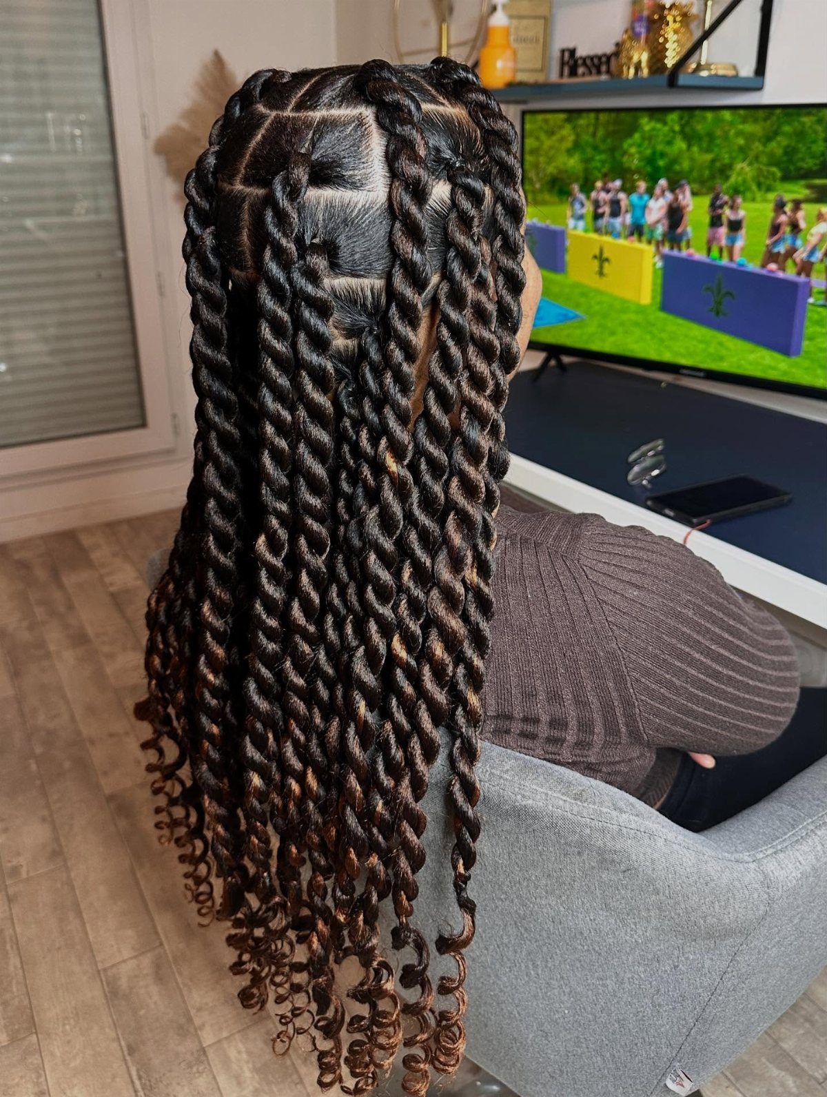 Long chunky twists with curled ends cascade down the back of seated person