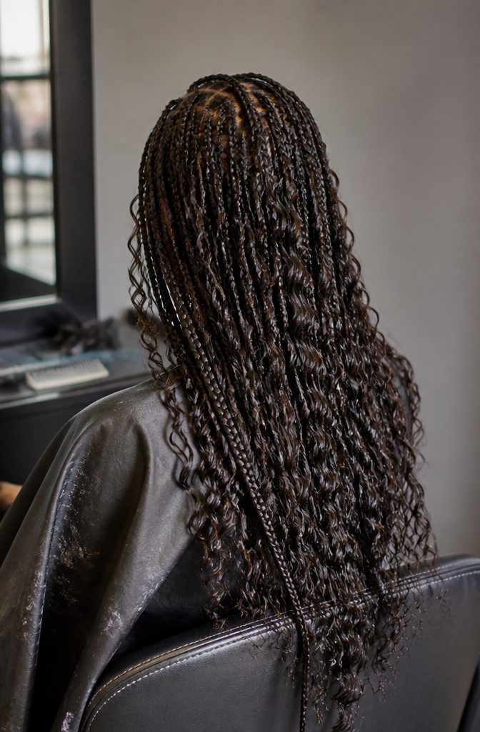 Deep curled hair extensions hanging beside braids with loose textured ends