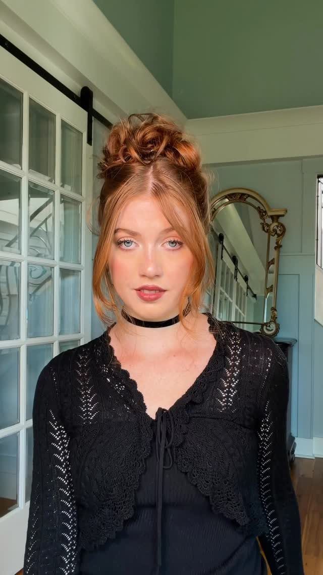 Woman wearing a high, loosely twisted red-haired bun with face-framing strands
