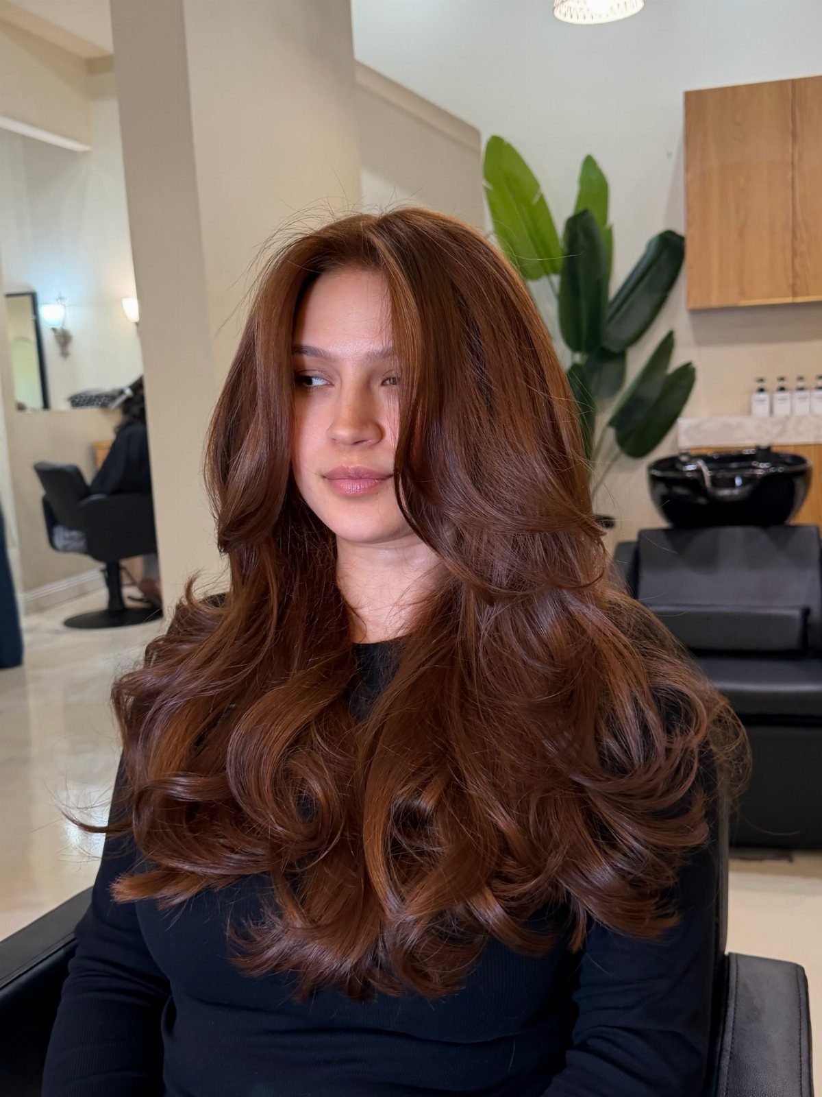 Woman with long, curled cinnamon-red hair seated in a salon
