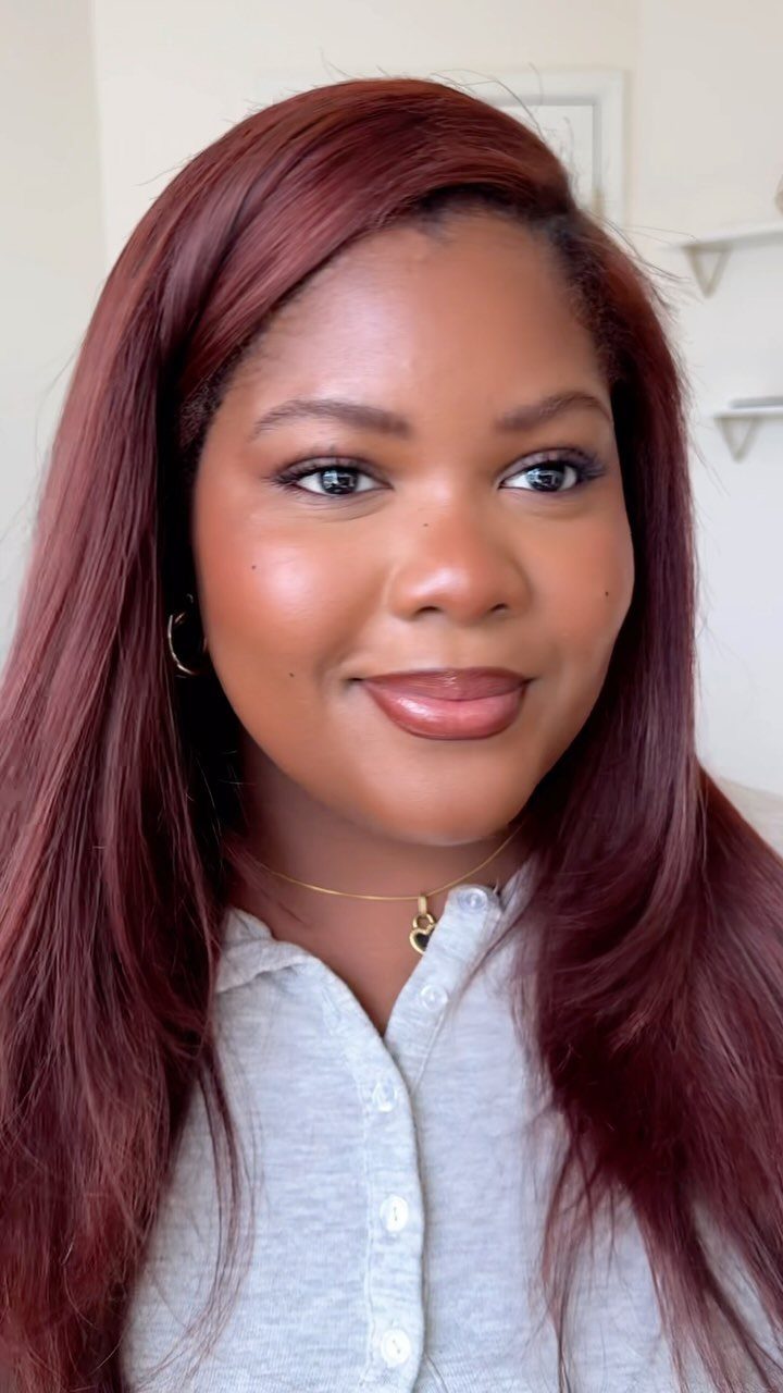 Woman with long, side-parted deep cherry-red hair and a light gray shirt