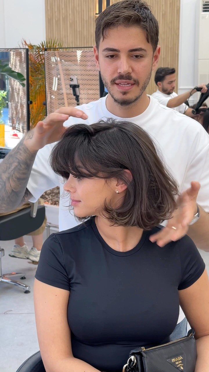 Woman with a dark French bob and bangs seated in a salon