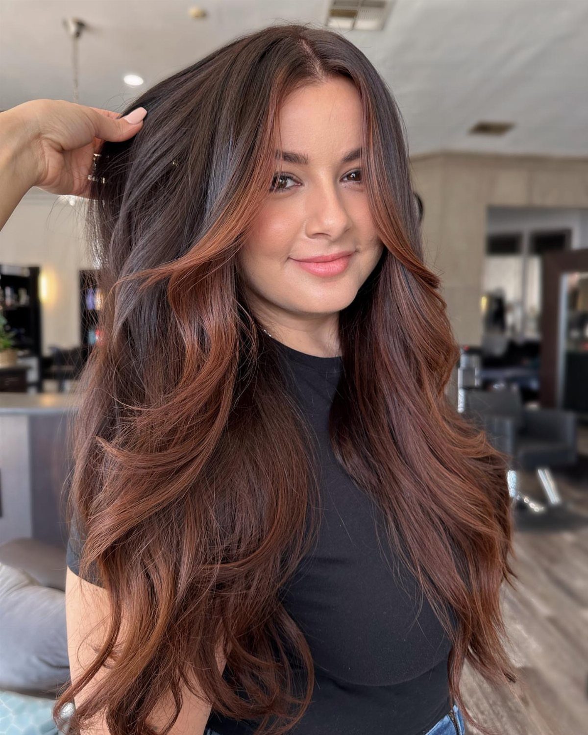 Woman with long, layered brown hair with warm reddish highlights in a salon
