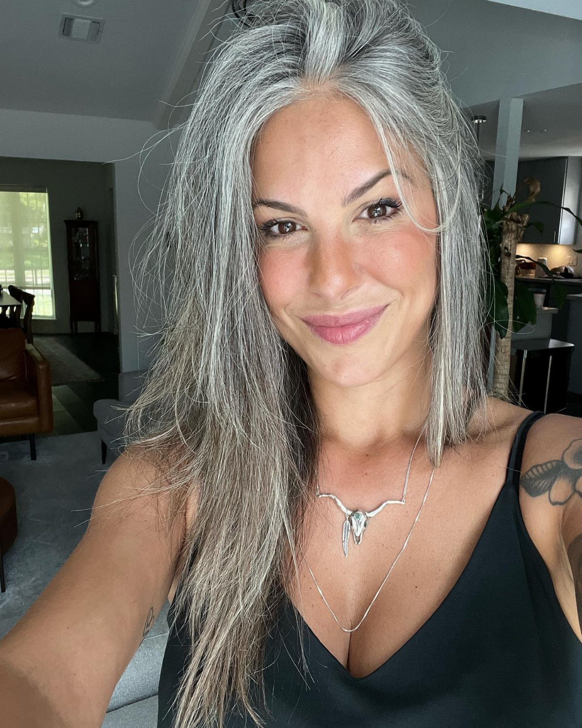 Woman smiles with long, naturally grey hair in a dark top