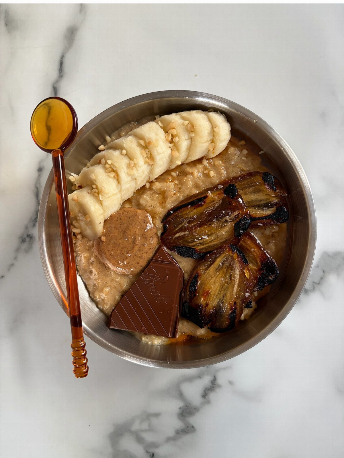 Oatmeal bowl topped with banana, browned fruit, nut butter, and chocolate