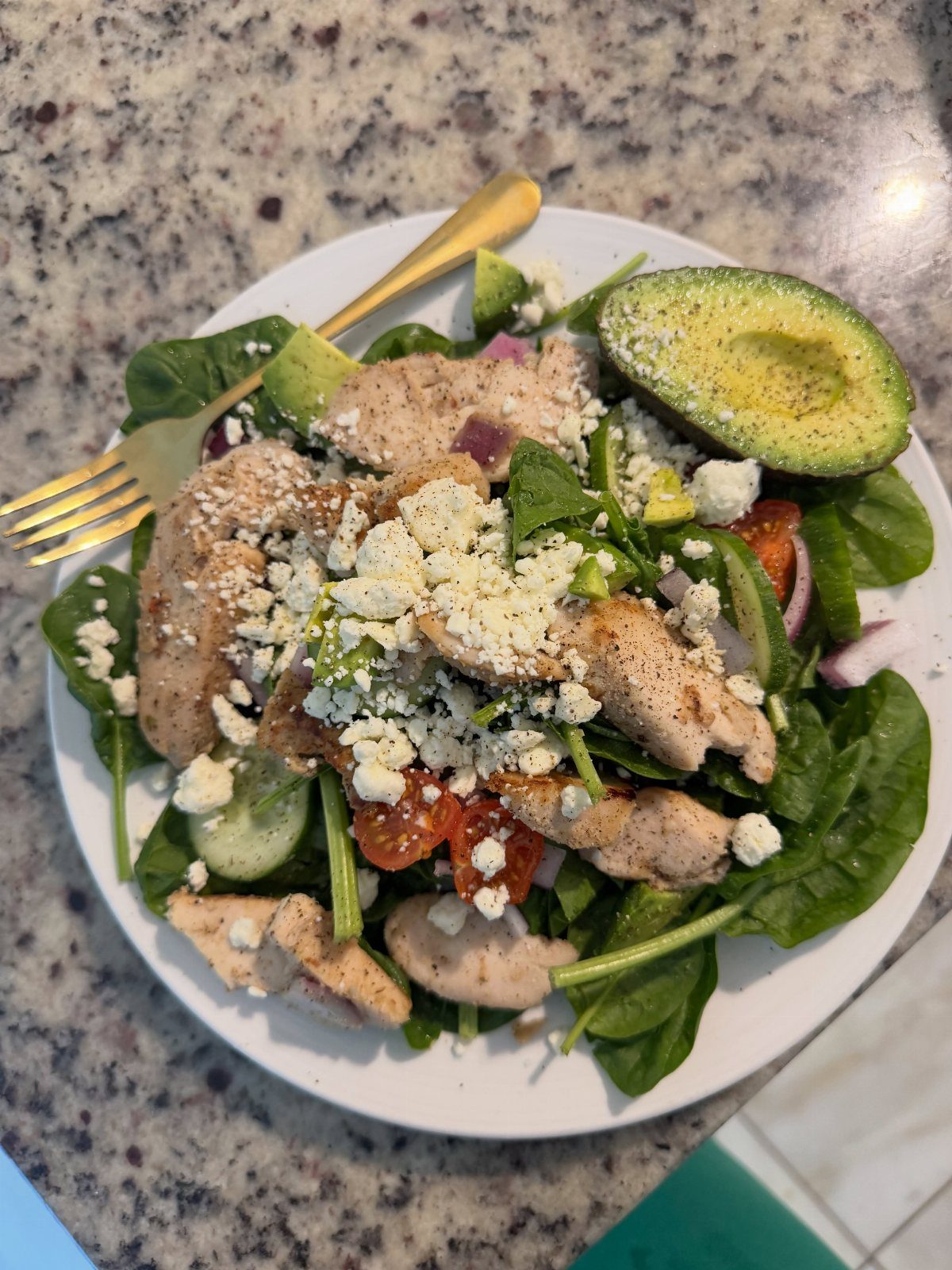 Spinach salad topped with chicken, avocado, cucumber, tomato, onion, and cheese